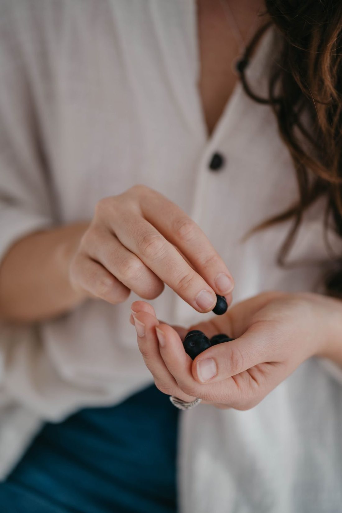 Close-up of hands holding a few dark berries against a cream shirt
