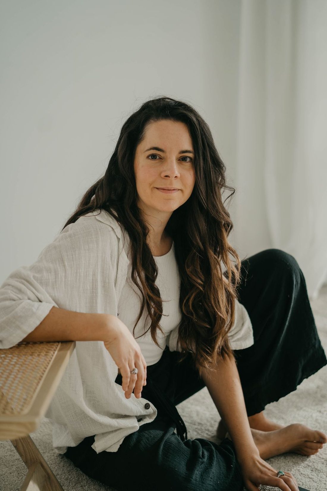 Angels Perez sitting on the floor beside a wooden chair, looking at the camera
