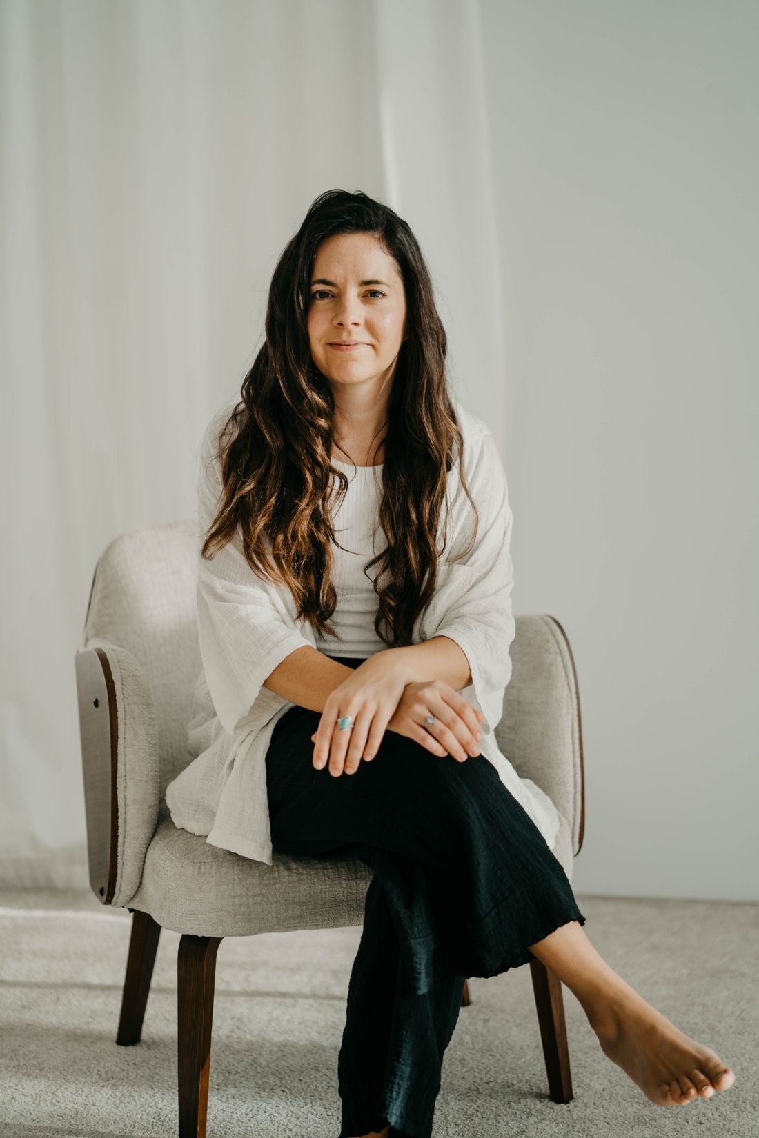 Angels Perez sitting in a pale armchair in a light room, looking at the camera with a calm smile