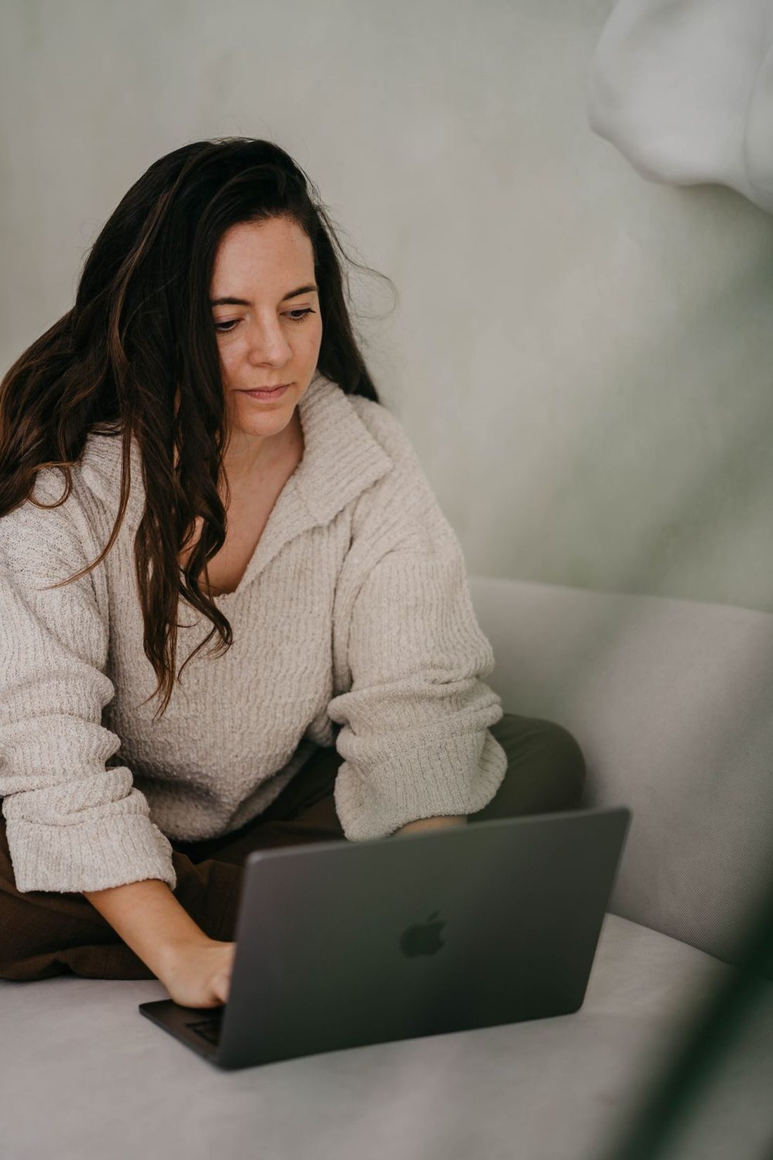 Angels Perez on a sofa in a cream jumper, looking at her laptop screen
