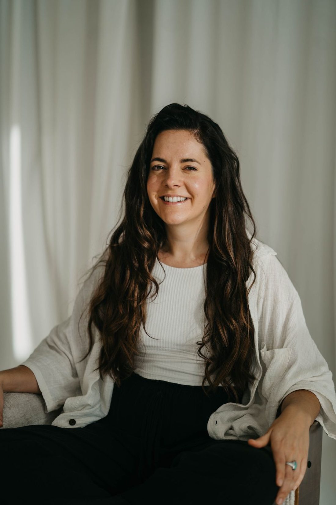 Angels Perez sitting in a pale armchair in a white top, smiling warmly